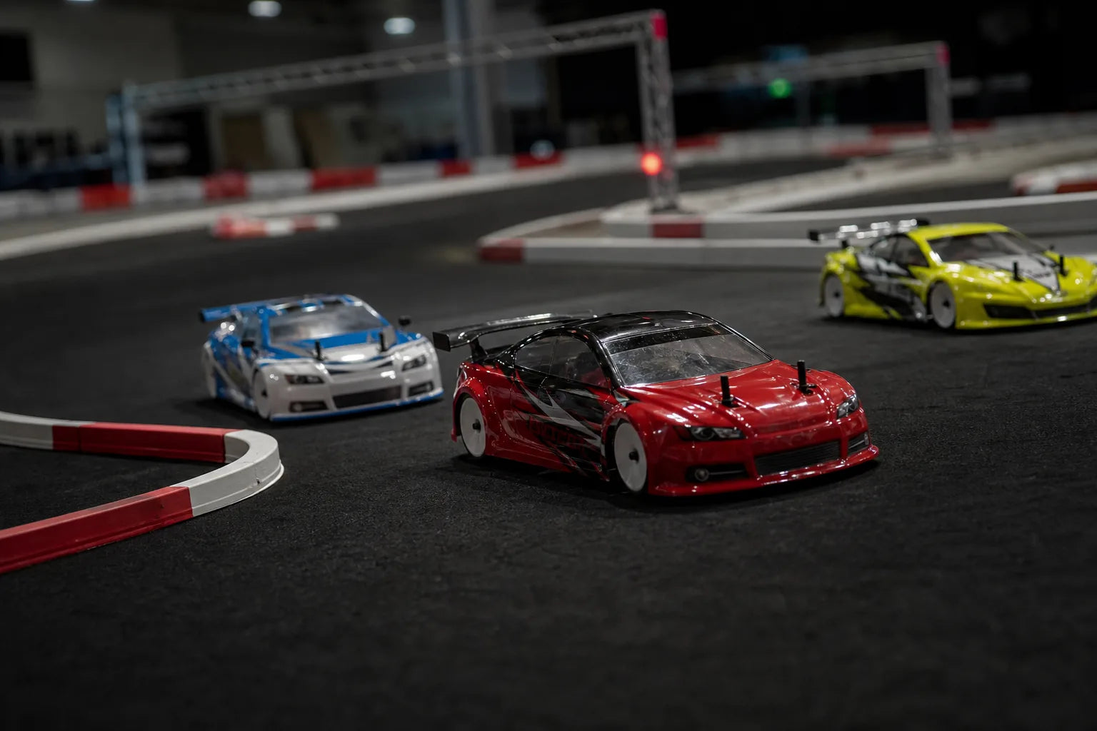 Three RC race cars battling through a corner on the indoor circuit at The Grid